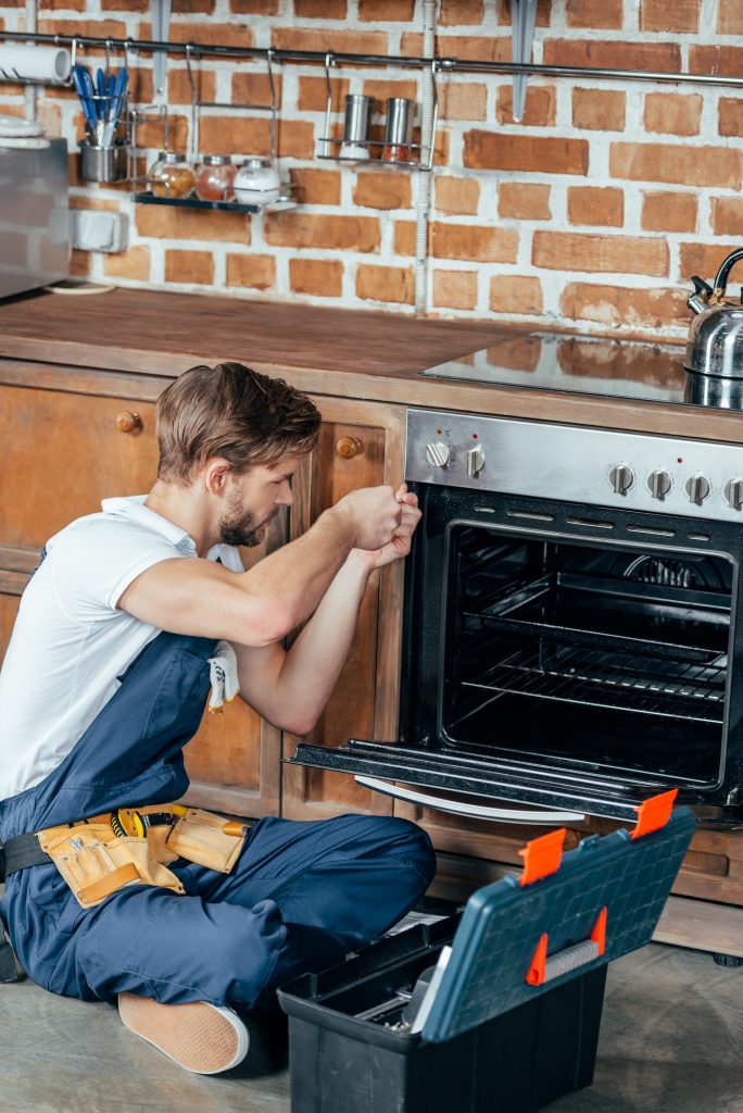 high angle view of young repairman fixing oven in kitchen